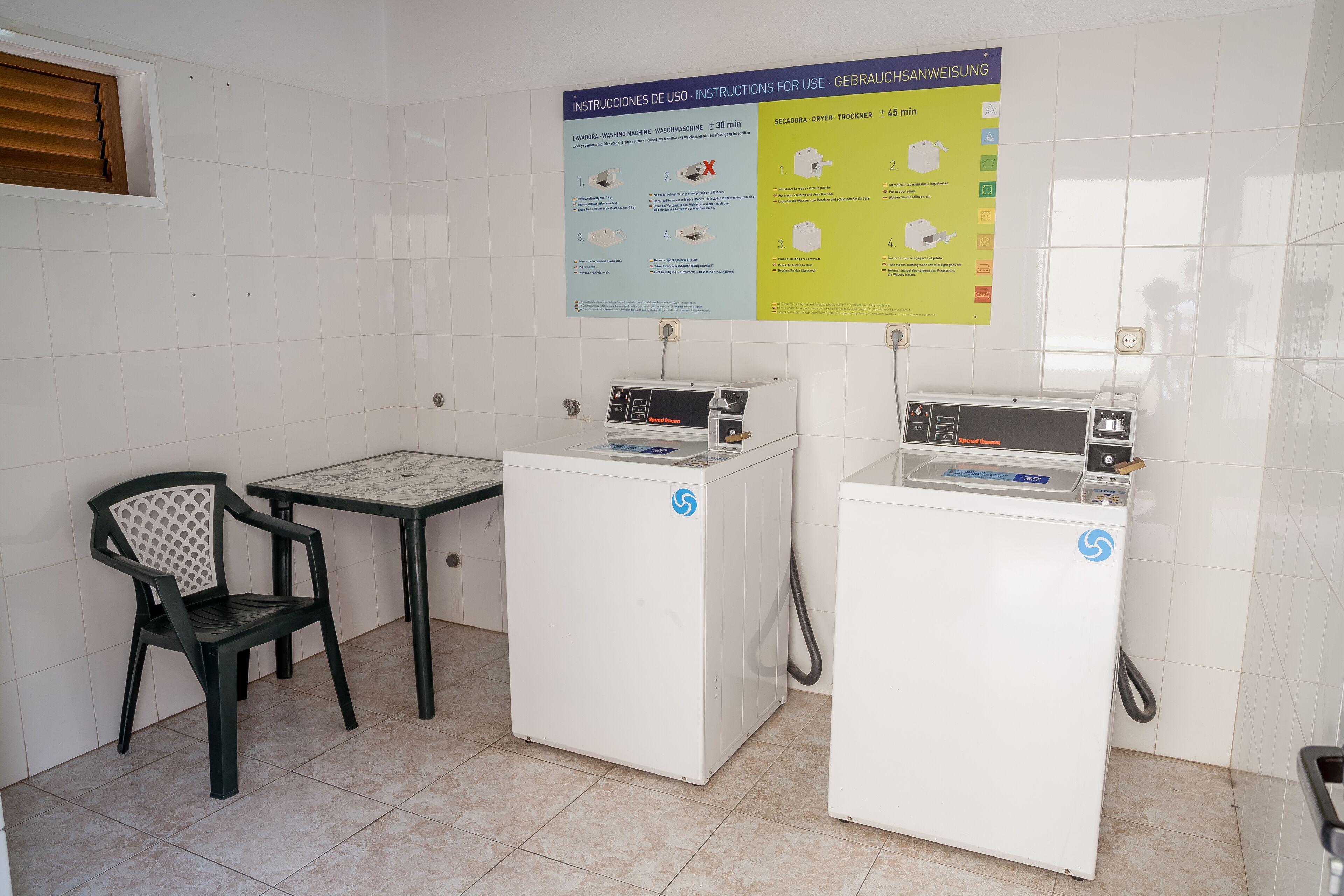 A laundry area with two washing machines, a chair, and a poster with instructions.