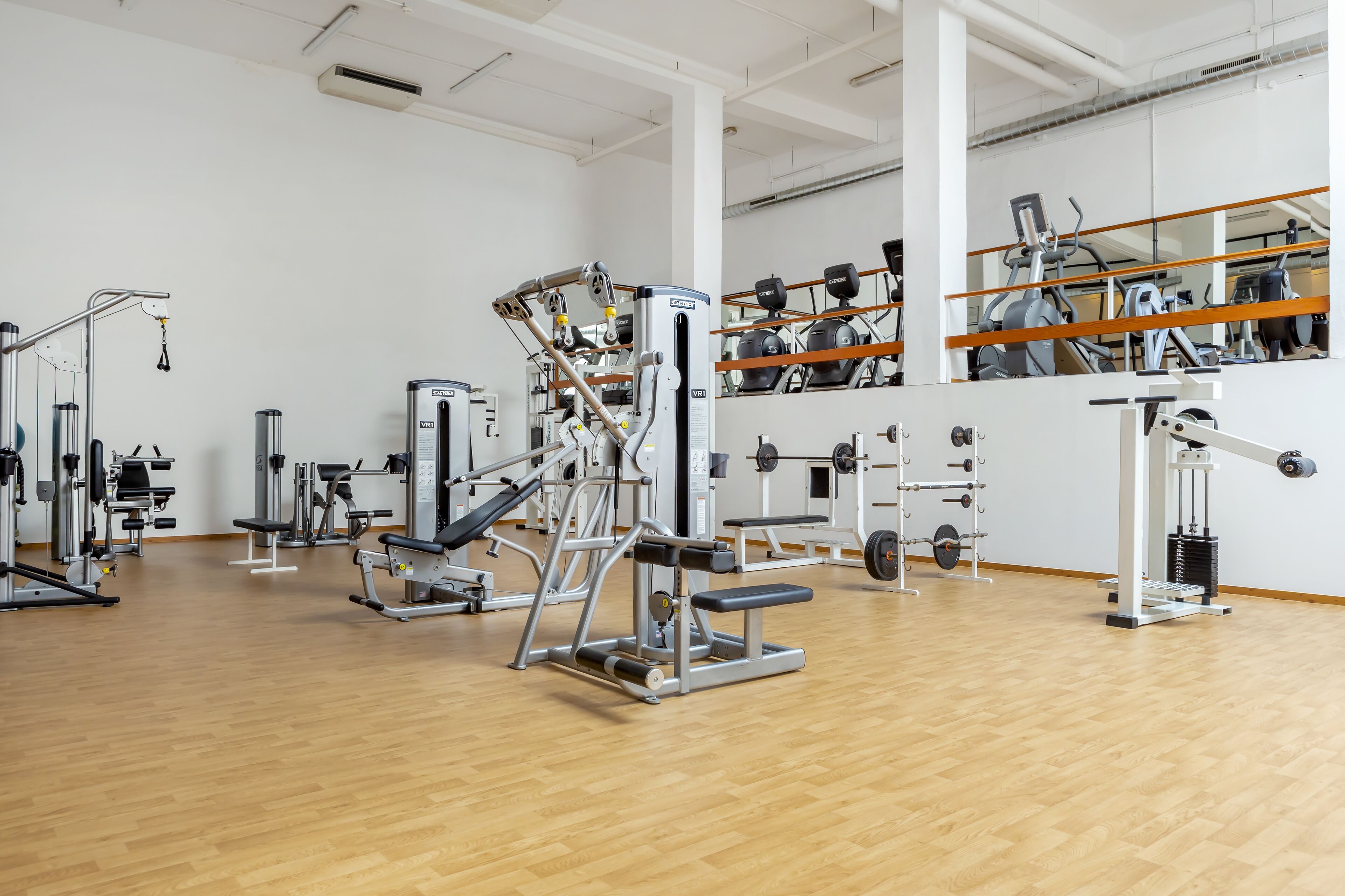 A gym with various exercise machines, mirrors on the walls, and a wooden floor.