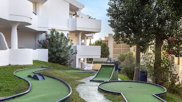 Un campo de mini golf con un sendero sinuoso, rodeado por un edificio blanco con balcones y vegetación.