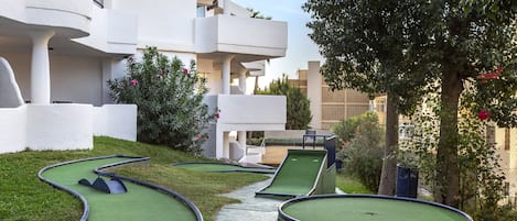 Un campo de mini golf con un sendero sinuoso, rodeado por un edificio blanco con balcones y vegetación.