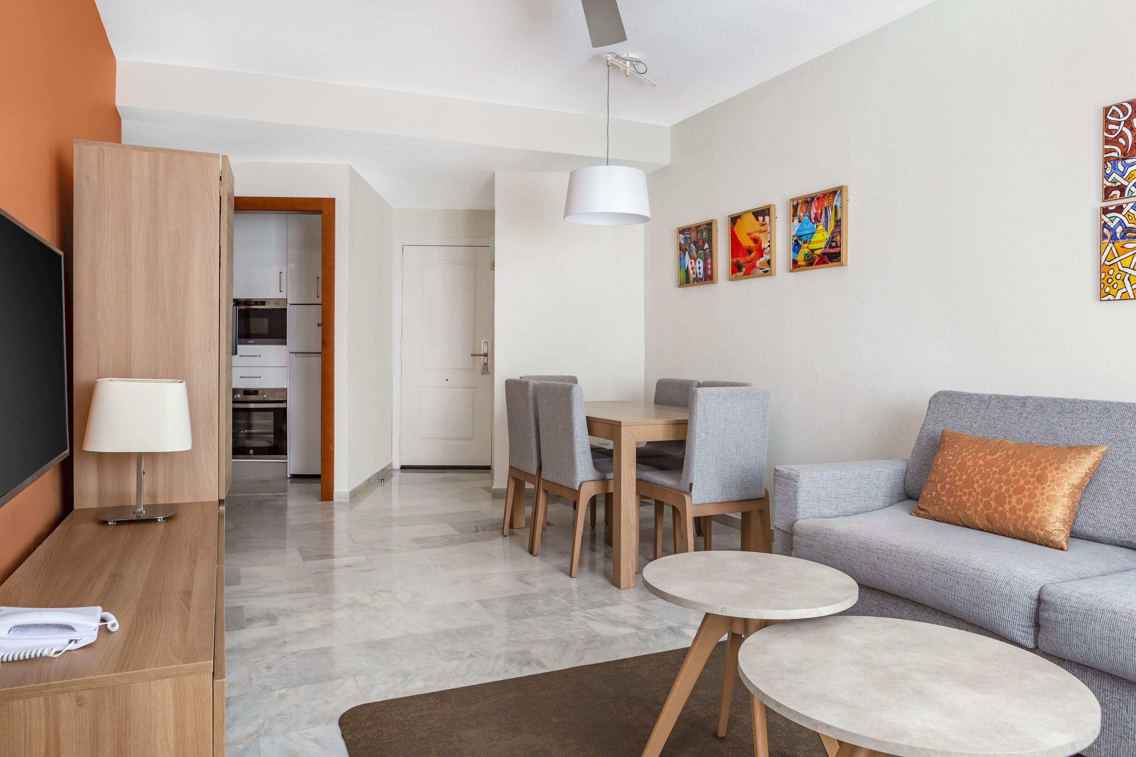 A modern living room with a sofa, two round tables, a TV, and a kitchen in the background.