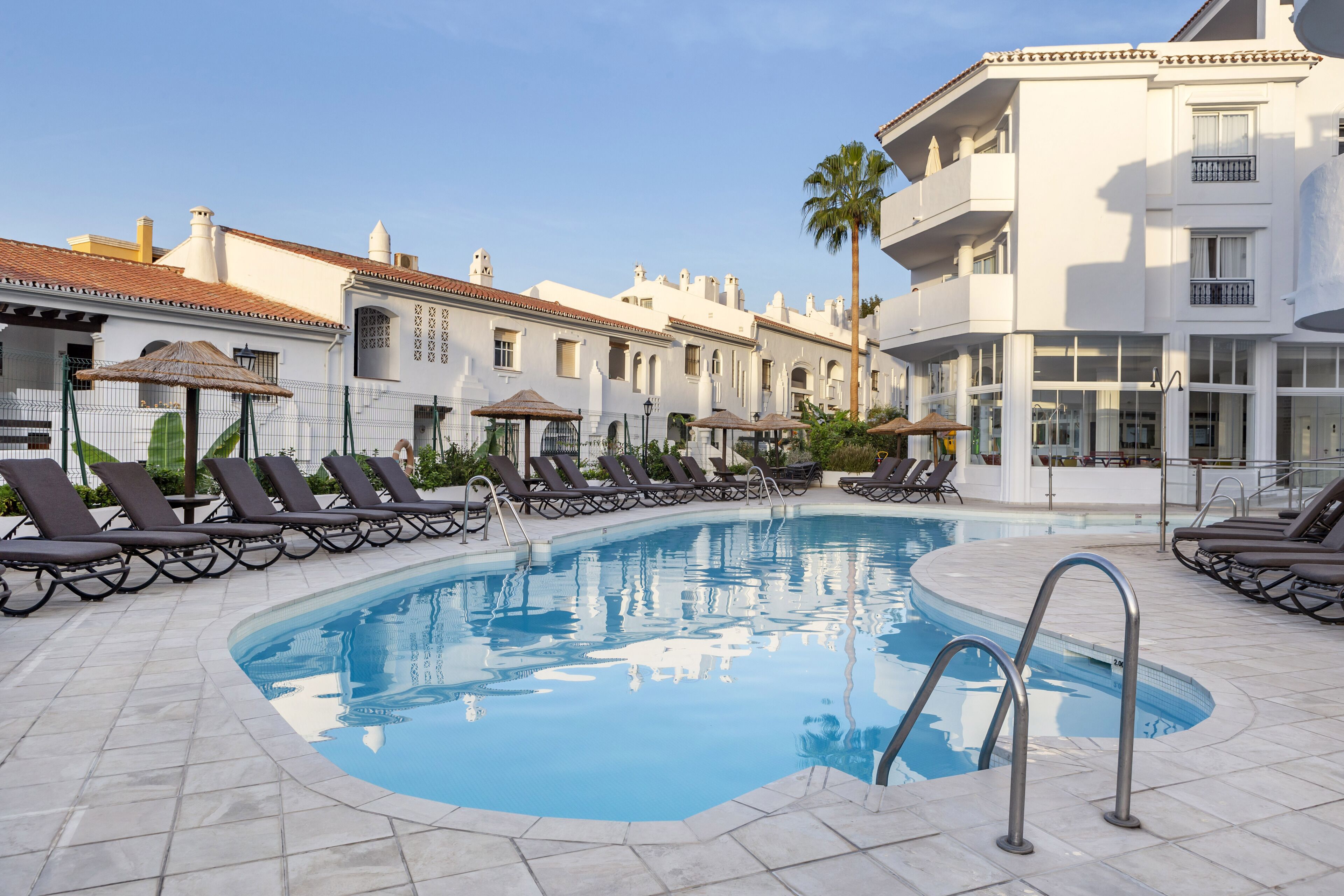 A swimming pool with lounge chairs and umbrellas, surrounded by buildings with balconies and windows.