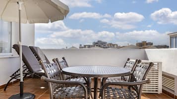 A round table with four chairs and a large umbrella on a tiled terrace.
