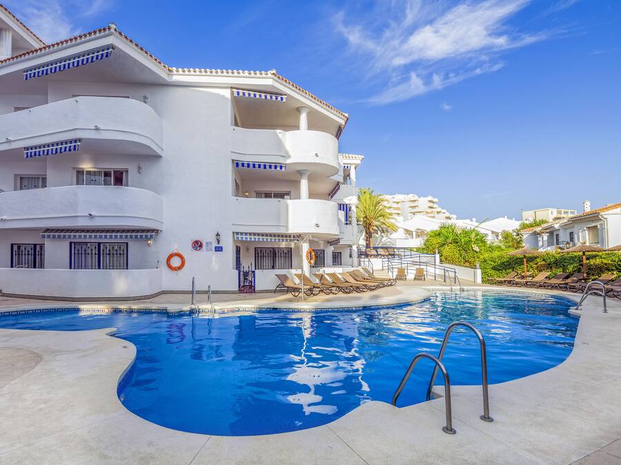 Un espace piscine avec un bâtiment blanc, de nombreux balcons et des chaises longues.