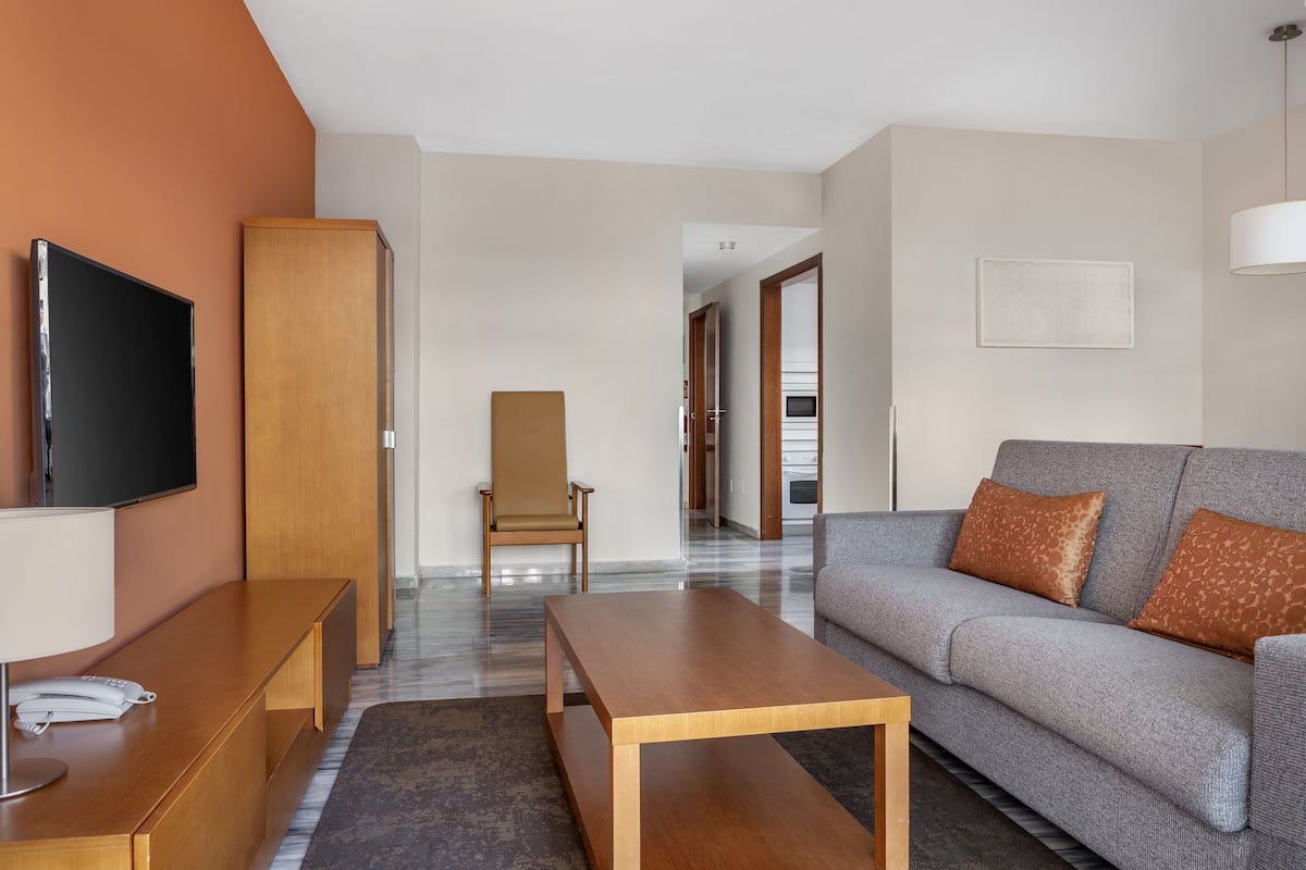 Un salon moderne avec un canapé, une table basse en bois, un téléviseur et un fauteuil.