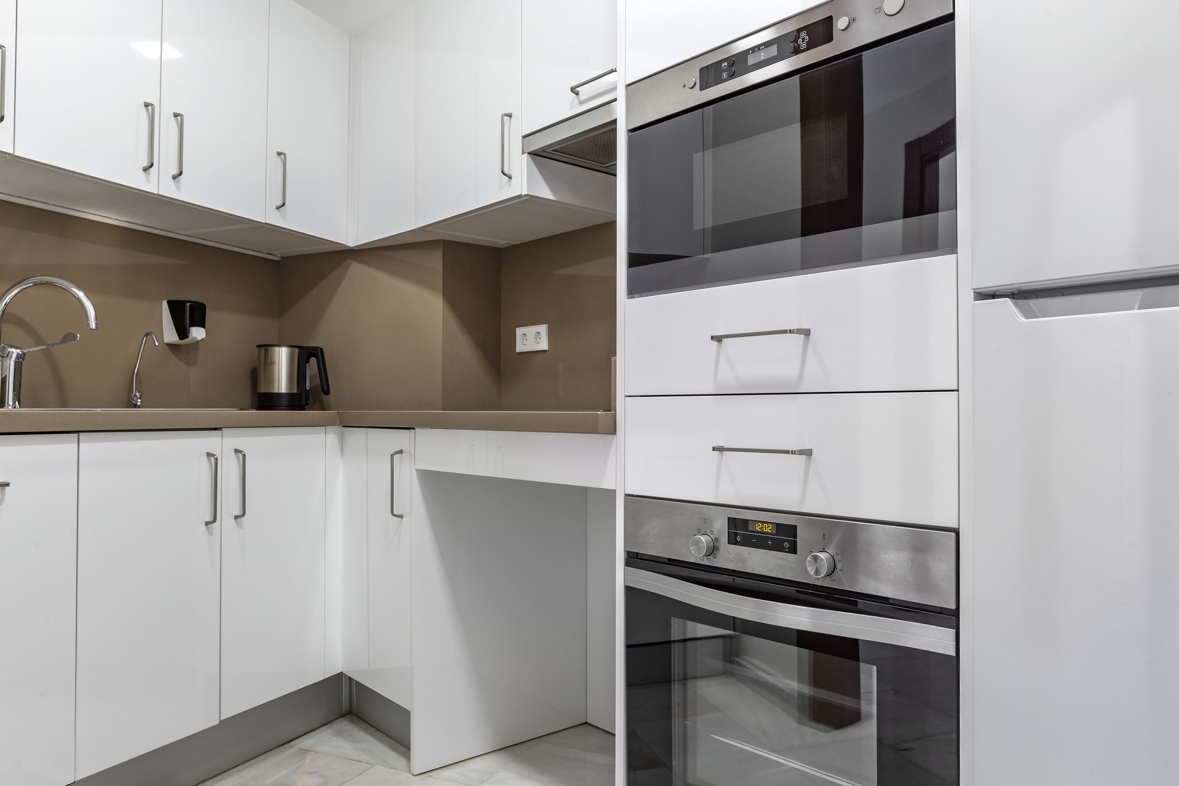 Une cuisine moderne avec des meubles blancs, des appareils en acier inoxydable et un comptoir de couleur beige.