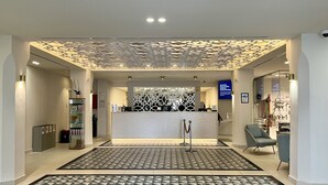 A modern reception area with a patterned floor, a reception desk, and a seating area with chairs. - Sahara Sunset (Benalmádena)