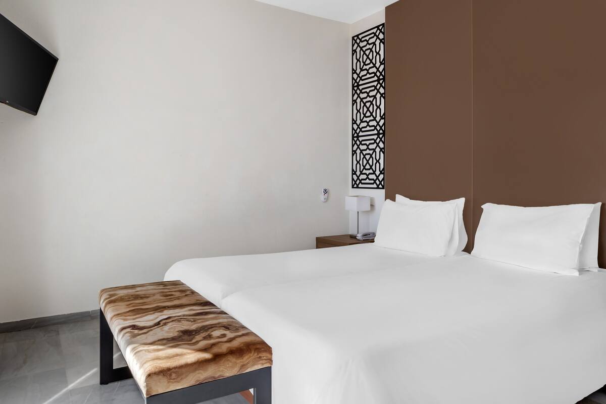 Une chambre d’hôtel avec un grand lit, un banc, un téléviseur fixé au mur et un paravent décoré.