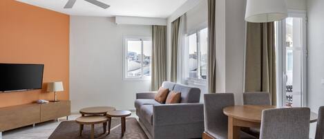A modern living room with a grey sofa, a wooden dining table, and a flat-screen TV.