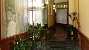 Un pasillo con alfombra estampada, plantas en macetas y un mural en la pared.