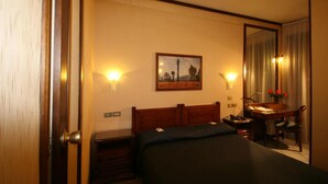 Una habitación de hotel con una cama, un escritorio, una silla, un cuadro en la pared y un espejo.