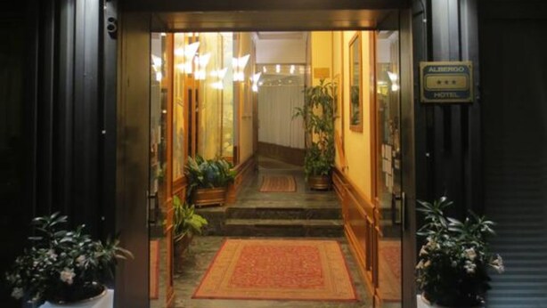 La entrada del Albergo Italia, con un letrero de neón, un camino alfombrado y plantas en macetas.