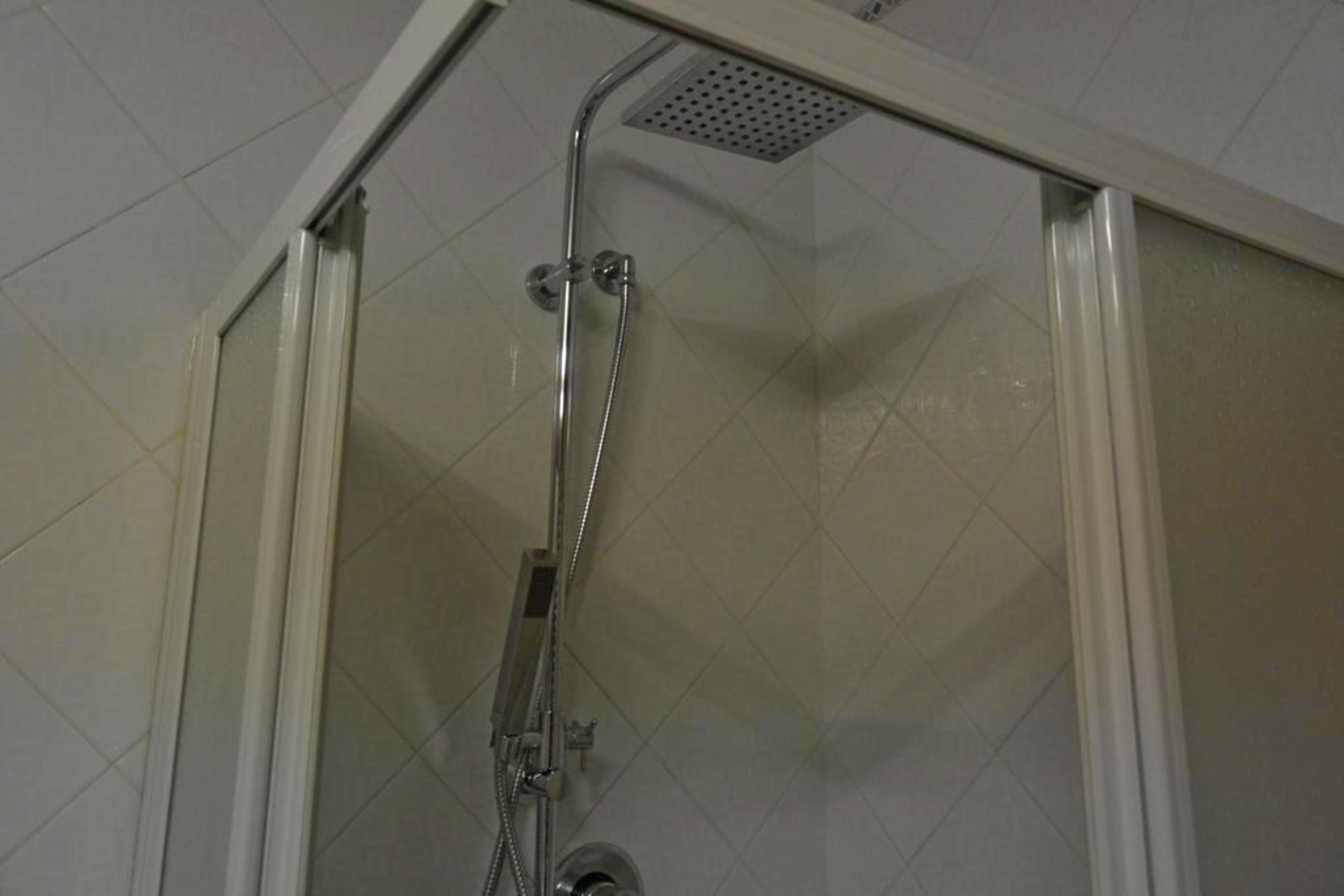 Ducha con cerramiento de vidrio, cabezal de ducha de mano y panel de control en la pared.