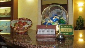Un mostrador de recepción de hotel con un bol de frutas de vidrio, un timbre y un letrero que indica el nombre del hotel y una calificación de tres estrellas.