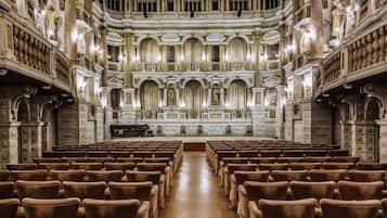 A grand hall with rows of brown chairs, ornate columns, and a central stage.