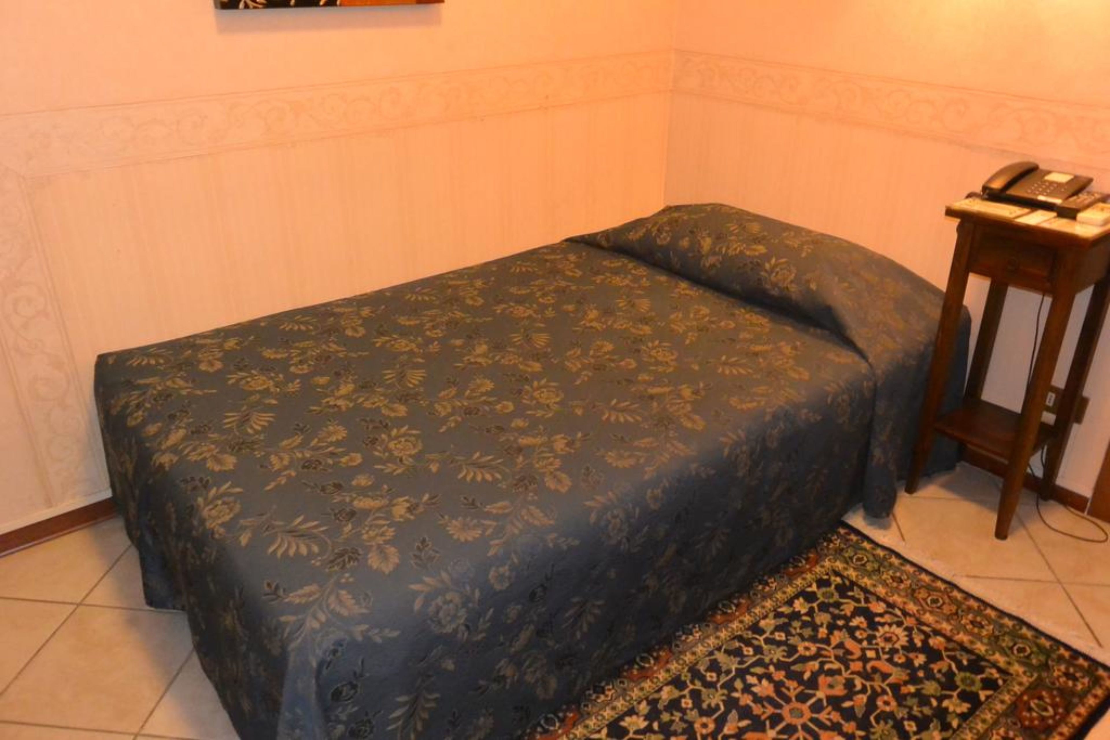 A small bedroom with a single bed, a nightstand with a telephone, and a patterned rug.