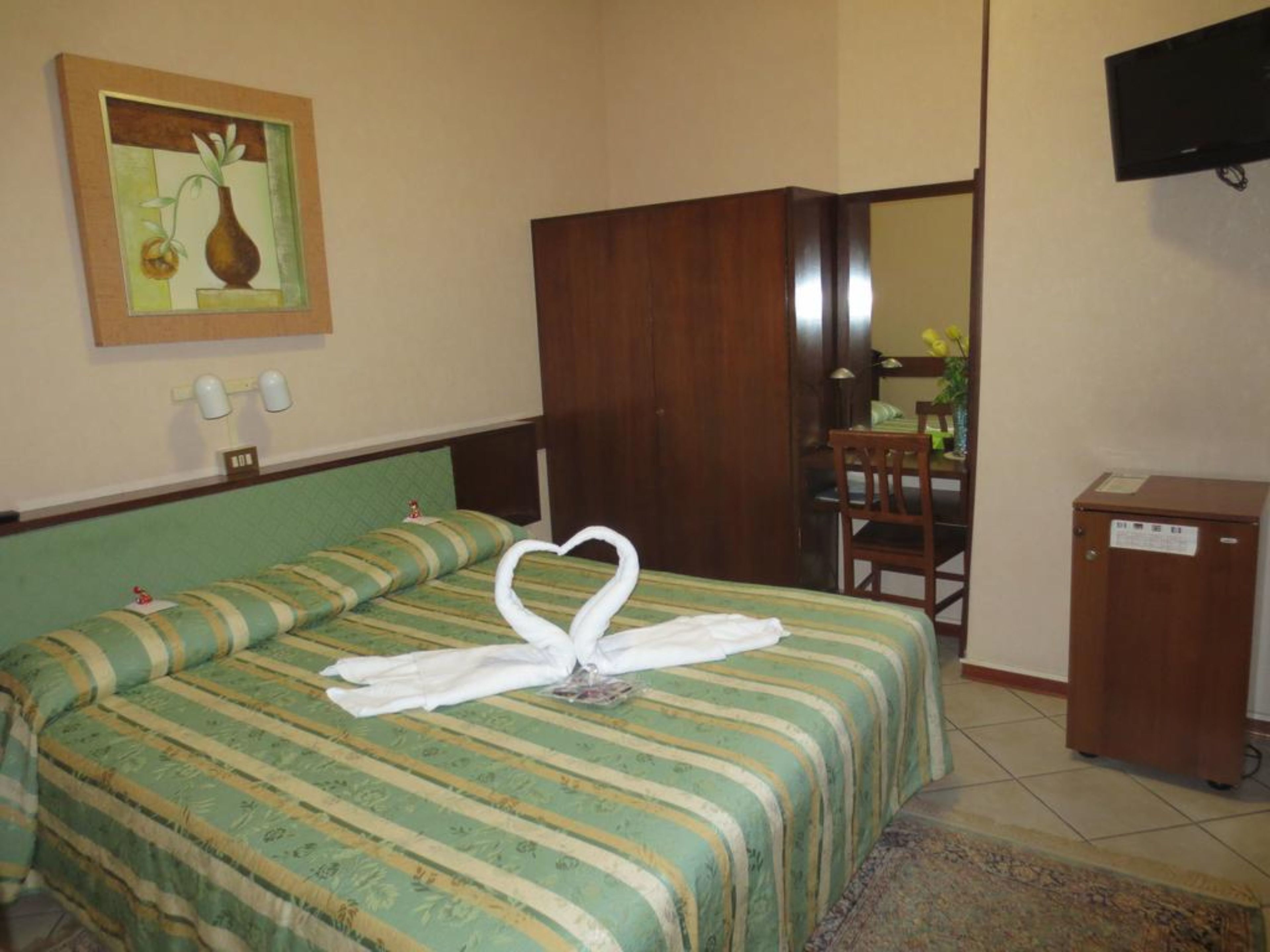 Ein Hotelzimmer mit Bett, einem Gemälde an der Wand, einem Schreibtisch und einem Fernseher.