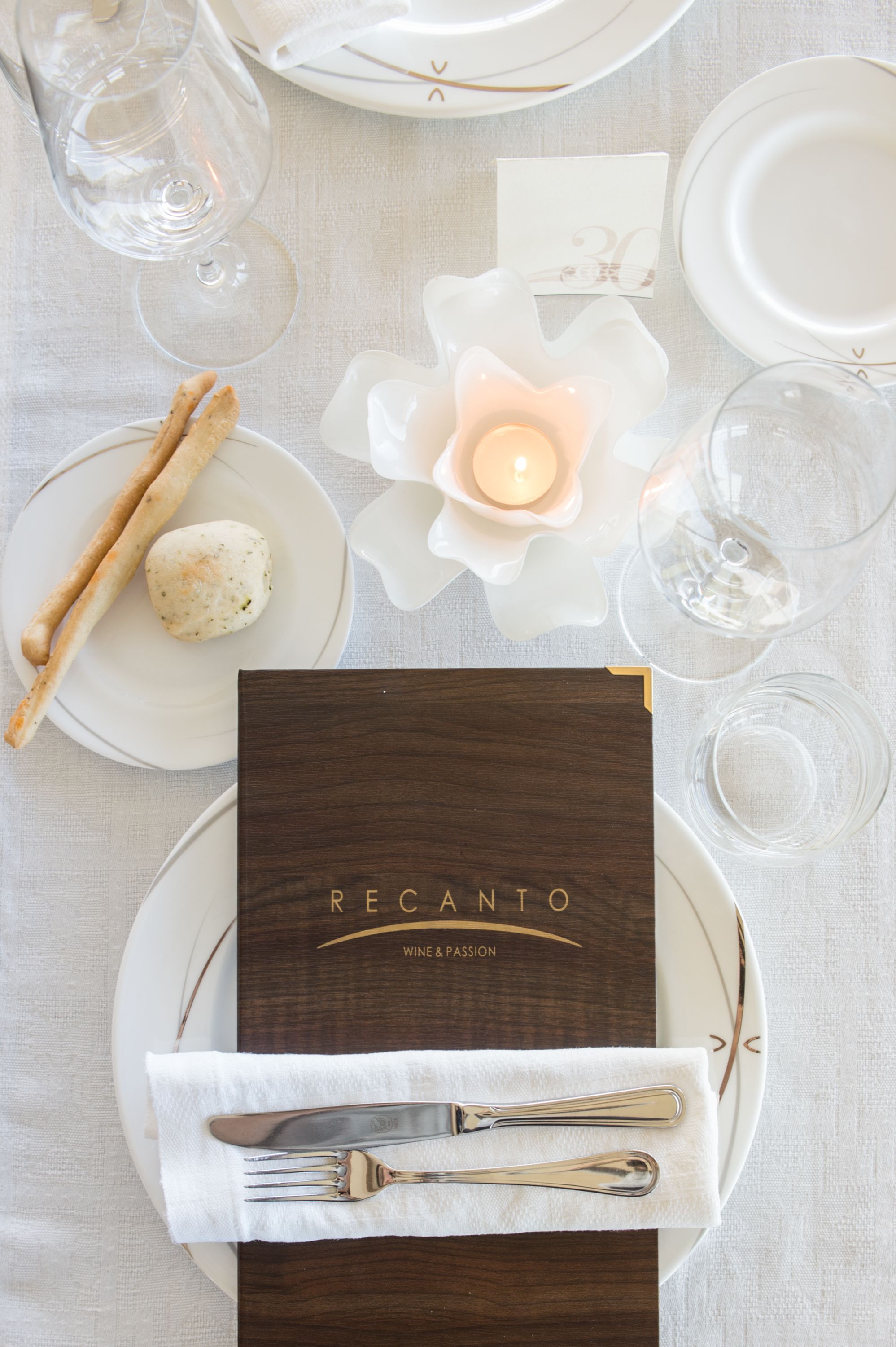 Une table dressée pour un repas, avec un menu intitulé « Recanto, vin et passion », comprenant des assiettes, des couverts et une bougie.