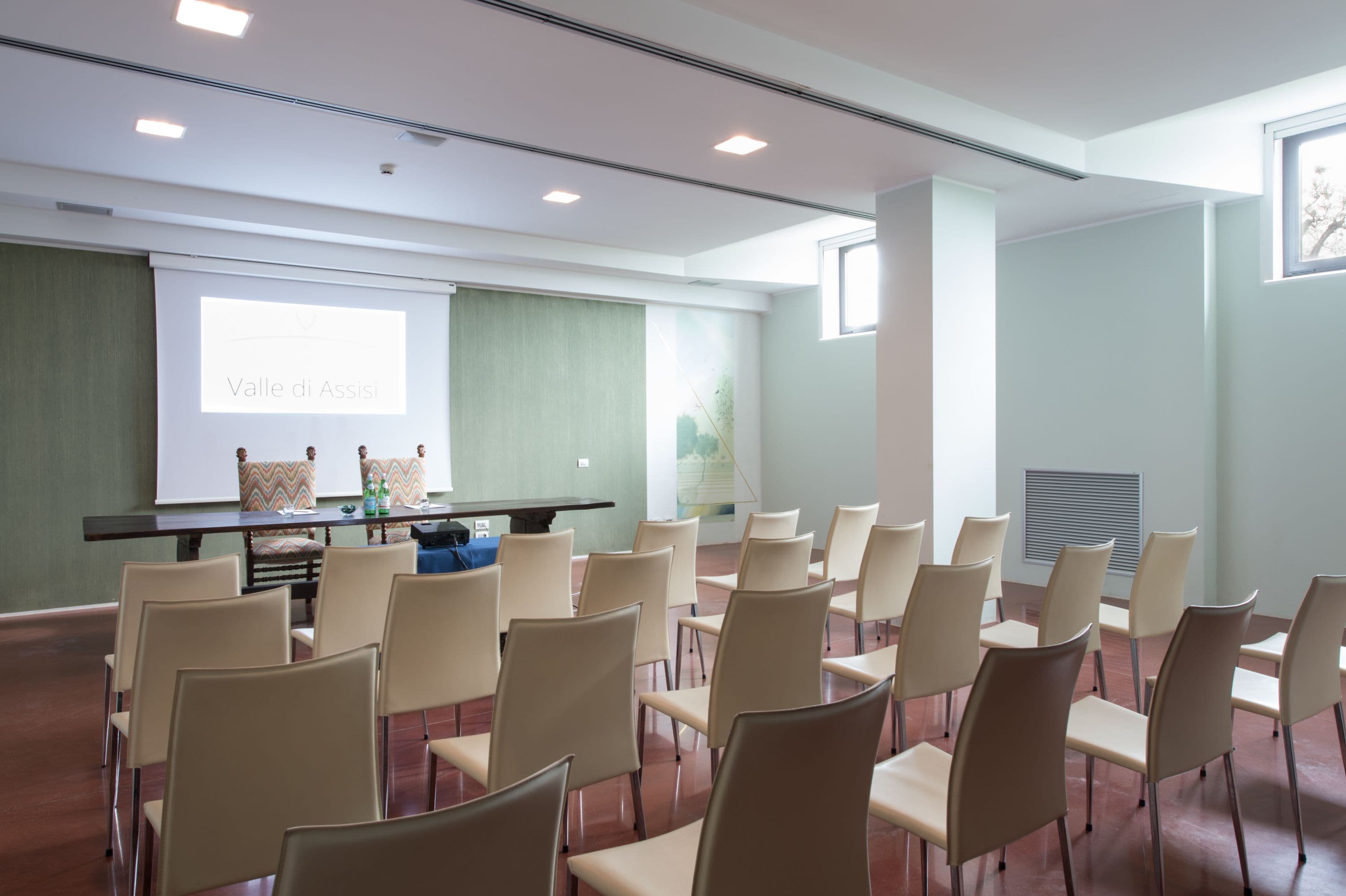 A conference room with a presentation screen, a table with chairs, and a large window.