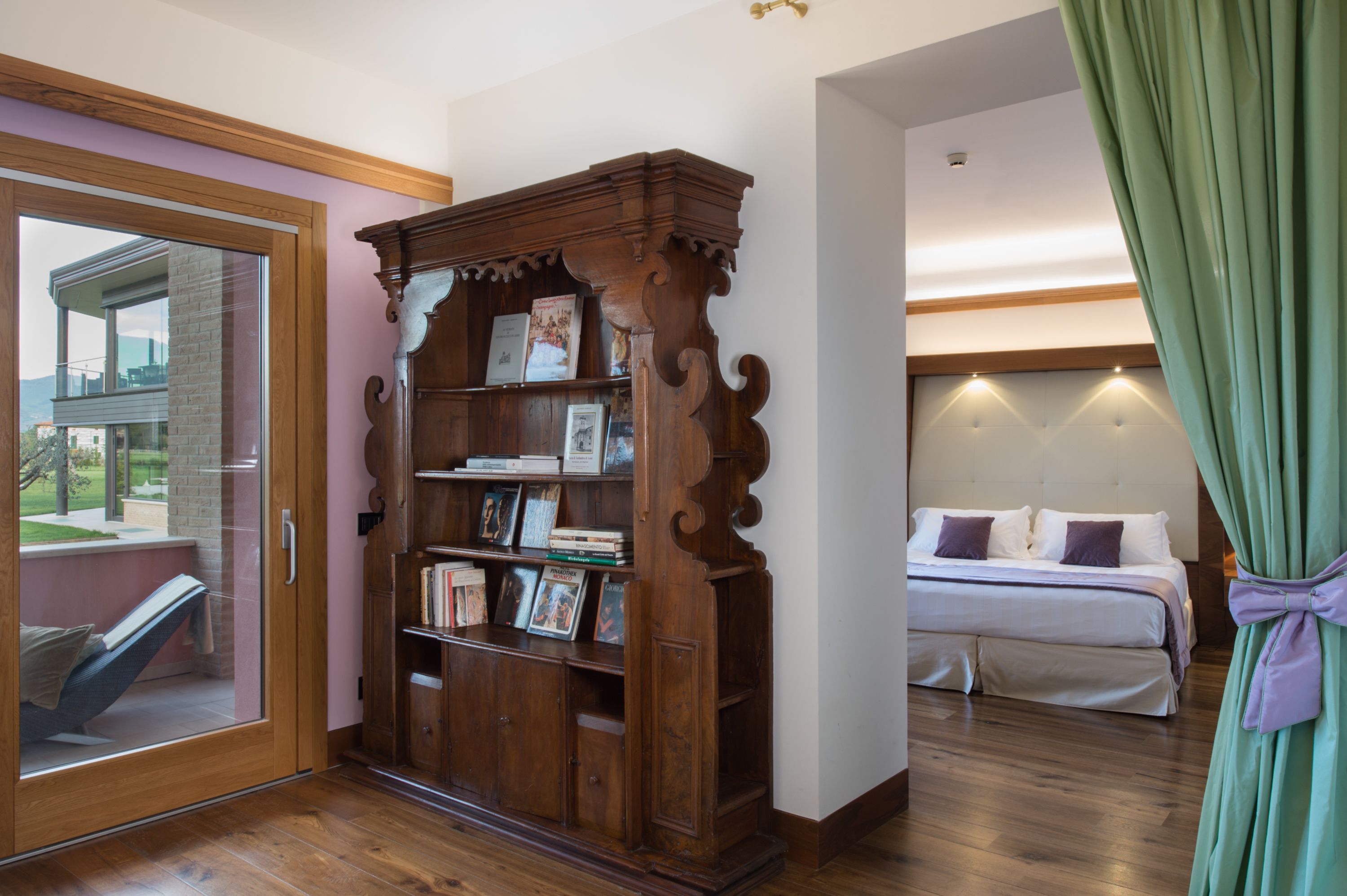 A bedroom with a wooden bookcase, a bed with white bedding, and a view through a glass door.