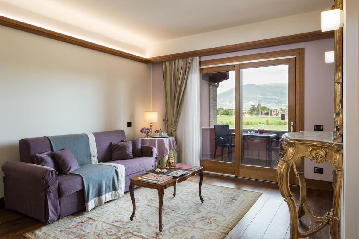 A living room with a purple sofa, a coffee table, and a view of a garden through a glass door.