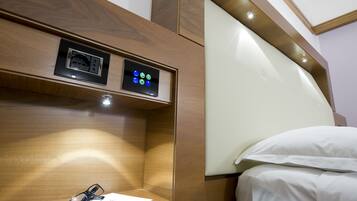 A hotel room with a wooden headboard, a bedside table with glasses and a notebook, and a control panel above the bed.