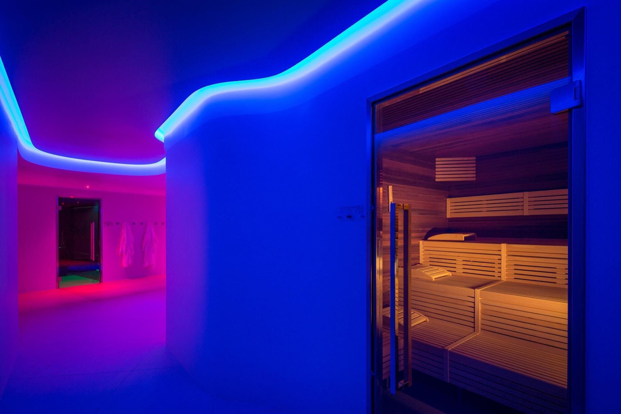 A modern room with a glass partition, a wooden bench, and a neon light strip along the ceiling.