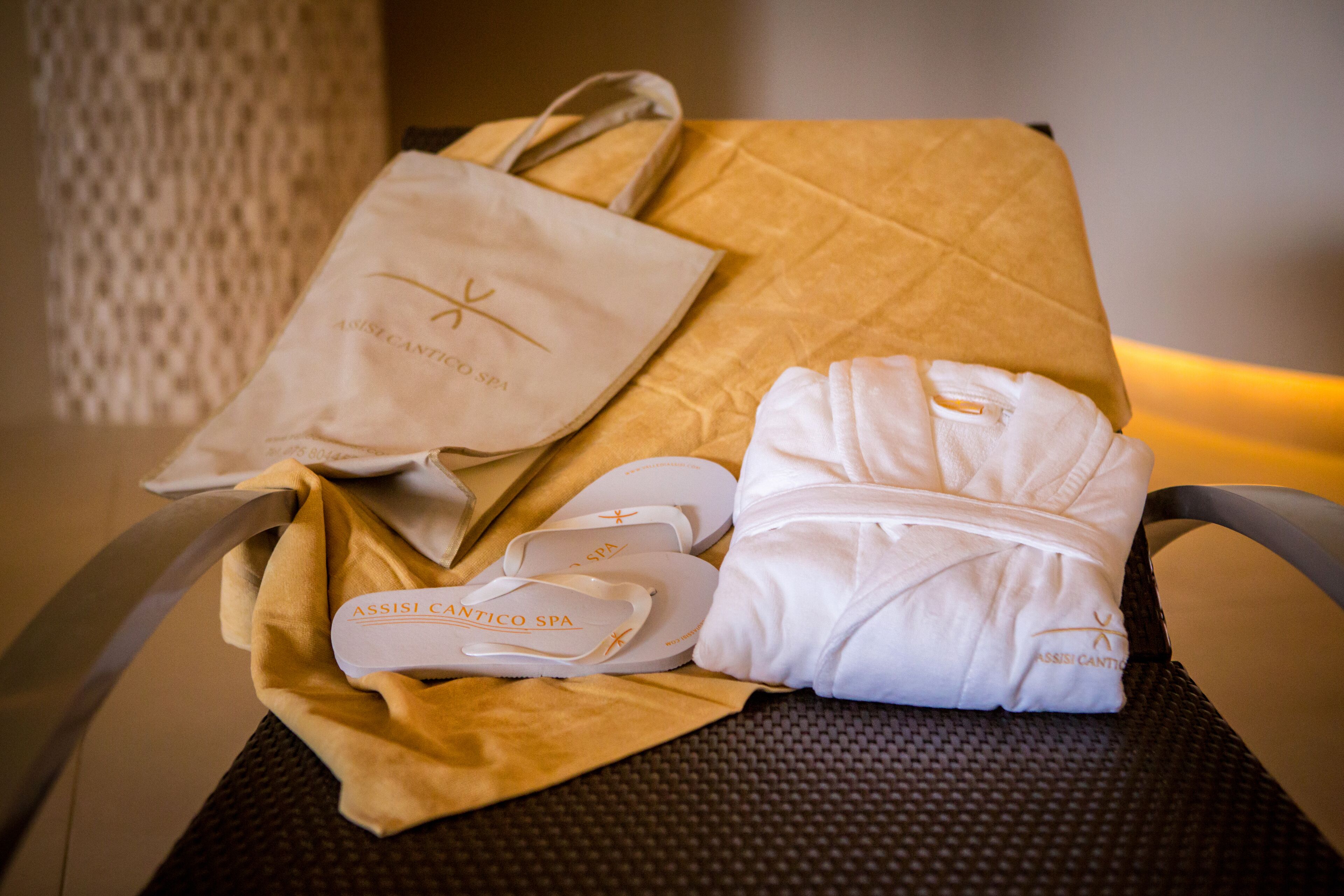 A set of spa slippers, a white robe, and a spa bag on a chair.