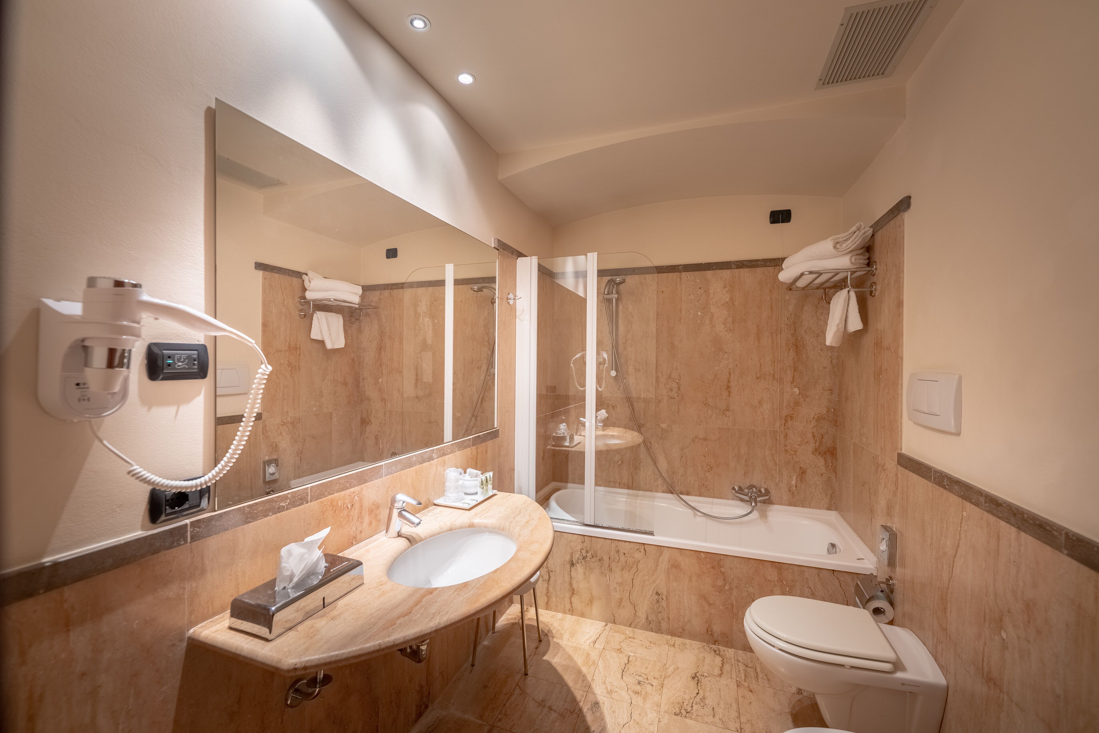 Une salle de bain moderne avec un meuble-lavabo en marbre, un grand miroir, un sèche-cheveux, une baignoire et des toilettes.