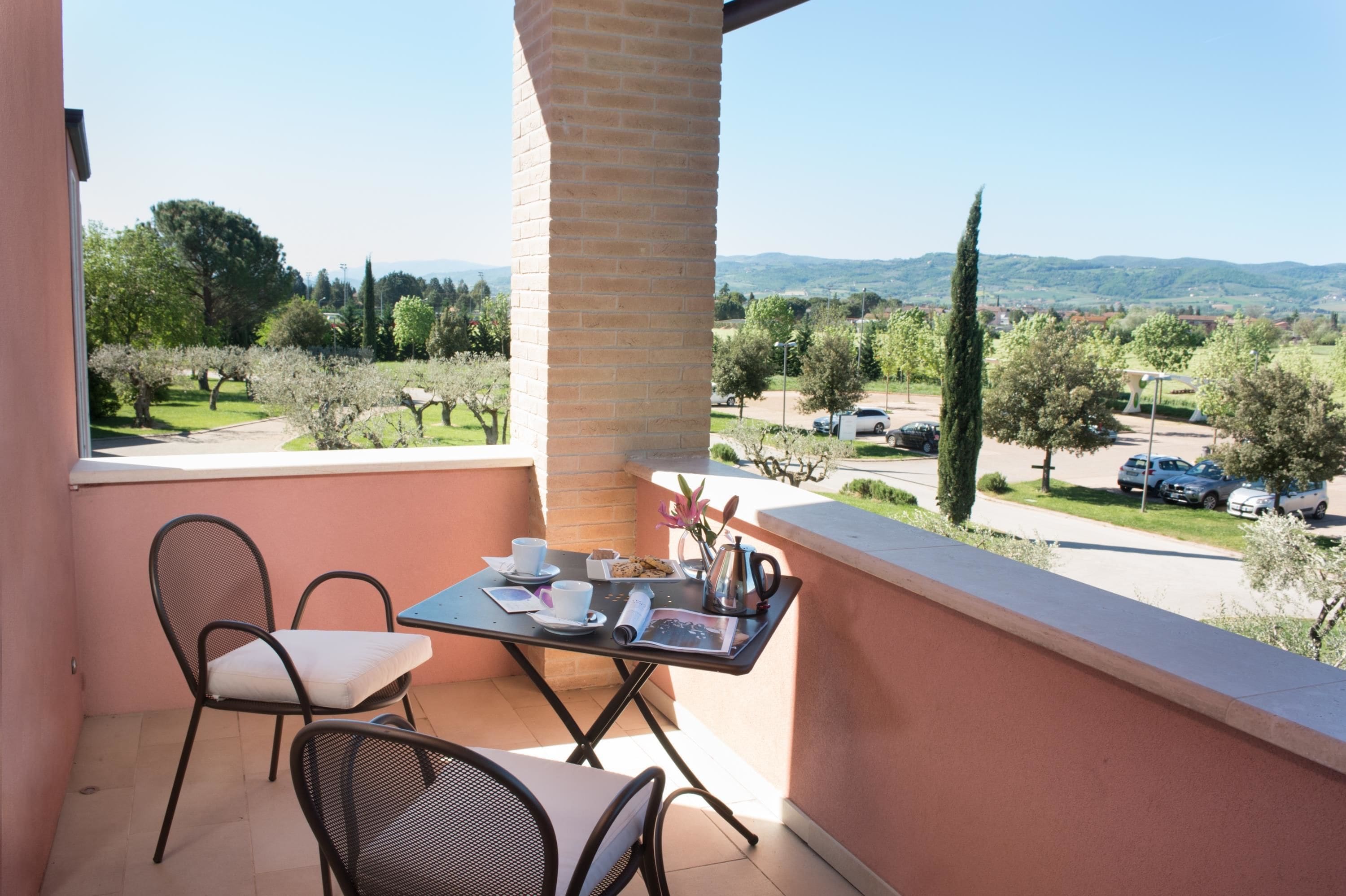 Un balcon avec une table et des chaises, donnant sur un paysage pittoresque avec des arbres et une route.