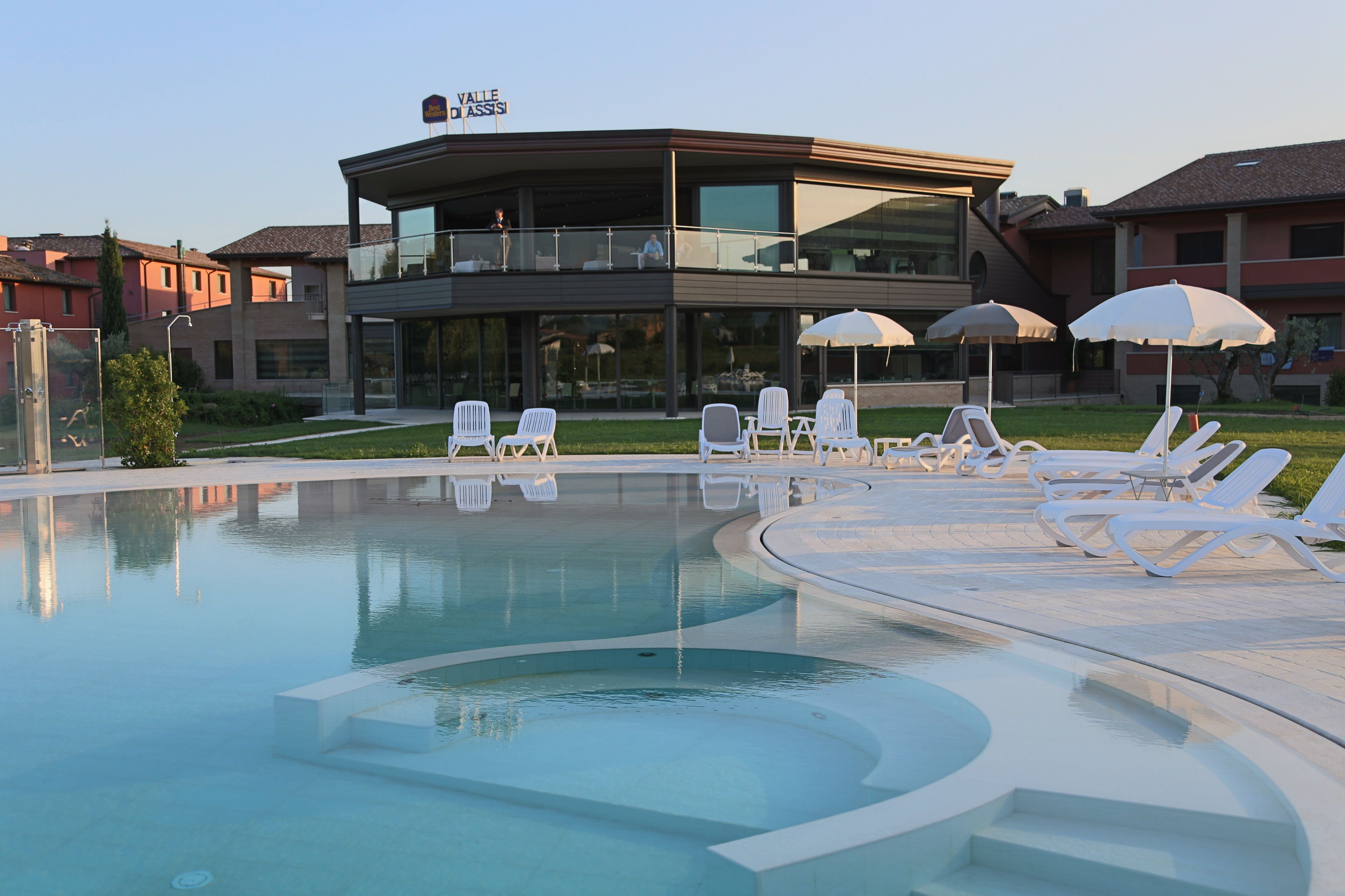 A modern hotel with a pool area, lounge chairs, and umbrellas.