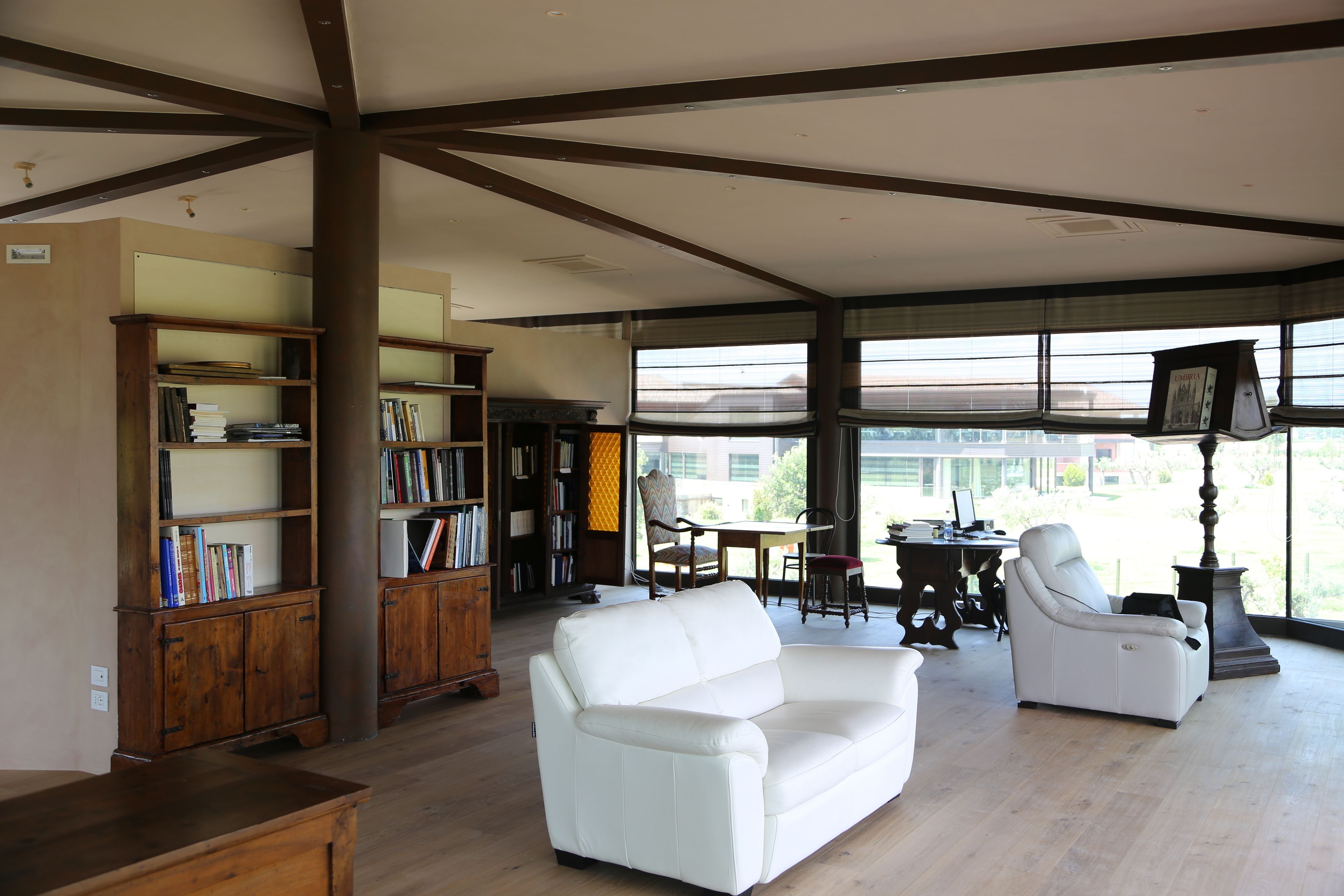 Uma sala de estar espaçosa com um sofá de couro branco, estantes de madeira e um espaço de jantar com mesa e cadeiras.