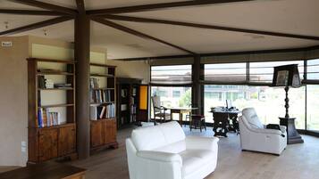 Uma sala de estar espaçosa com um sofá de couro branco, estantes de madeira e um espaço de jantar com mesa e cadeiras.