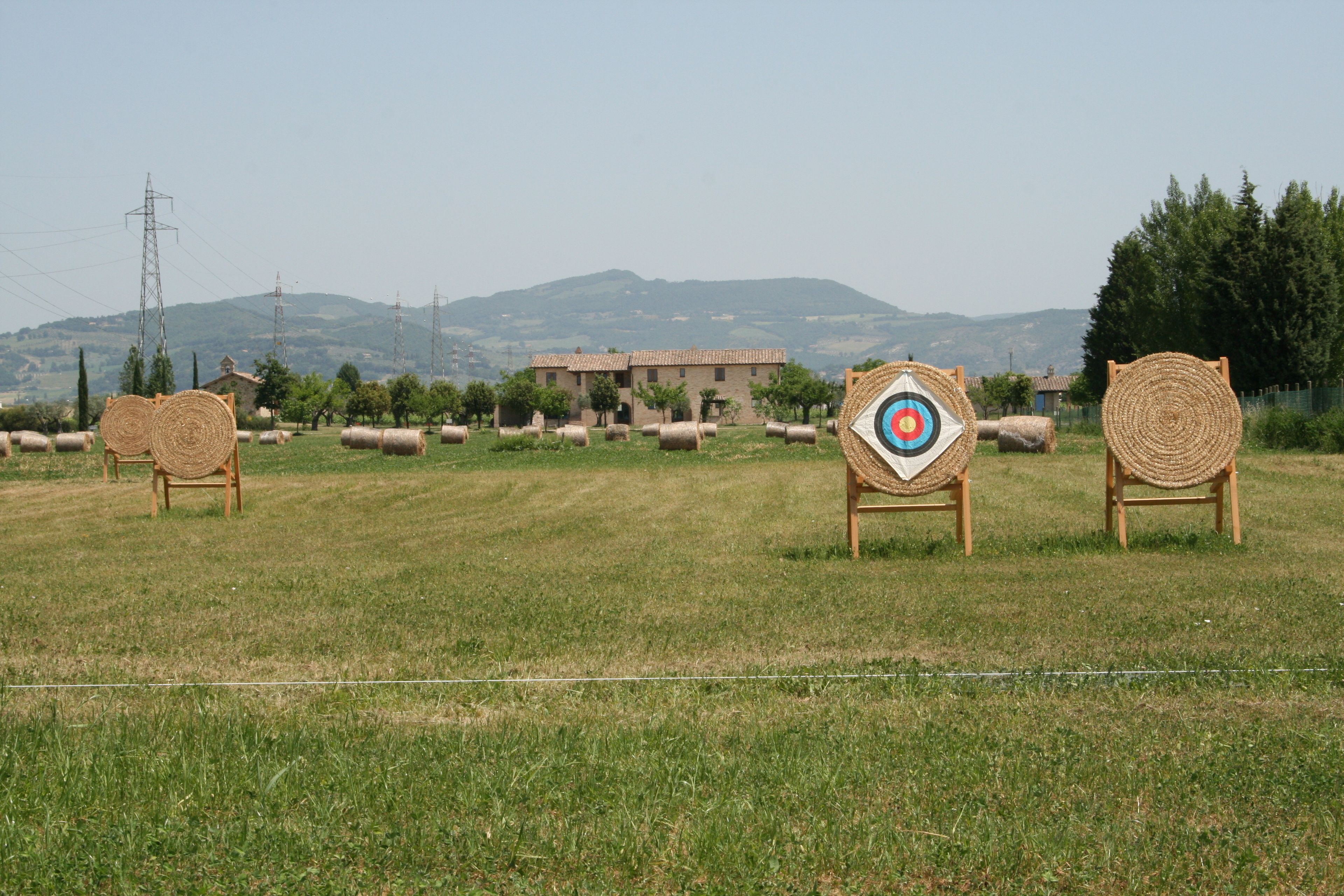 Paesaggio rurale con balle di fieno, un bersaglio e un edificio sullo sfondo.