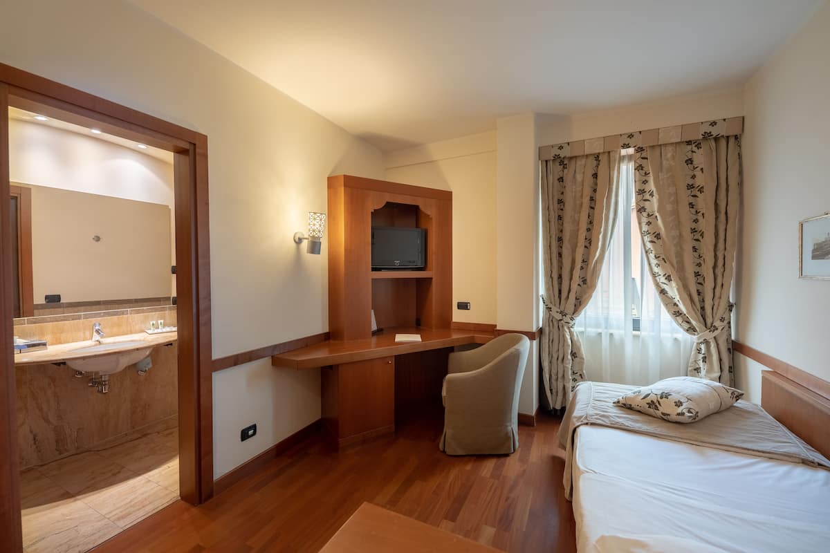 A hotel room with a wooden desk, a bed, a TV, and a bathroom with a sink and mirror.