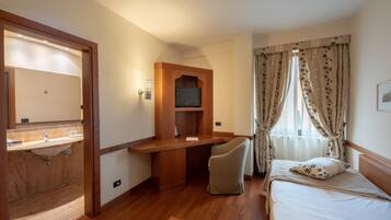 A hotel room with a wooden desk, a bed, a TV, and a bathroom with a sink and mirror.