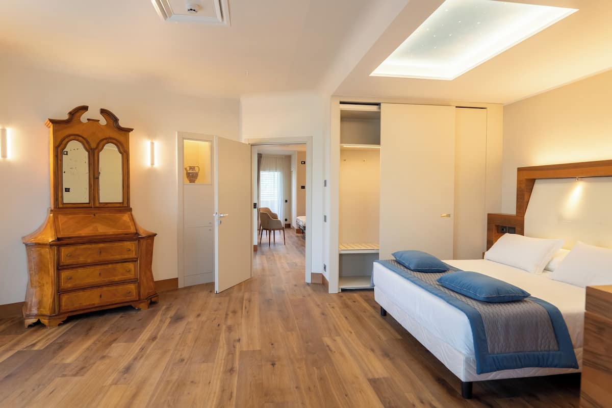 A hotel room with a wooden dresser, a bed with blue bedding, and a walk-in closet.