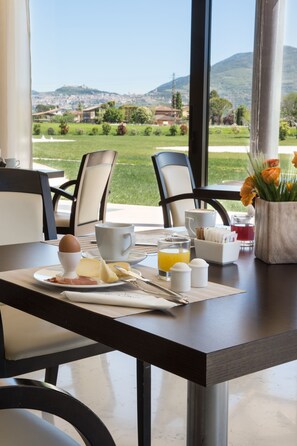 Una mesa de desayuno con huevos, queso y jugo, con vistas a un paisaje pintoresco.