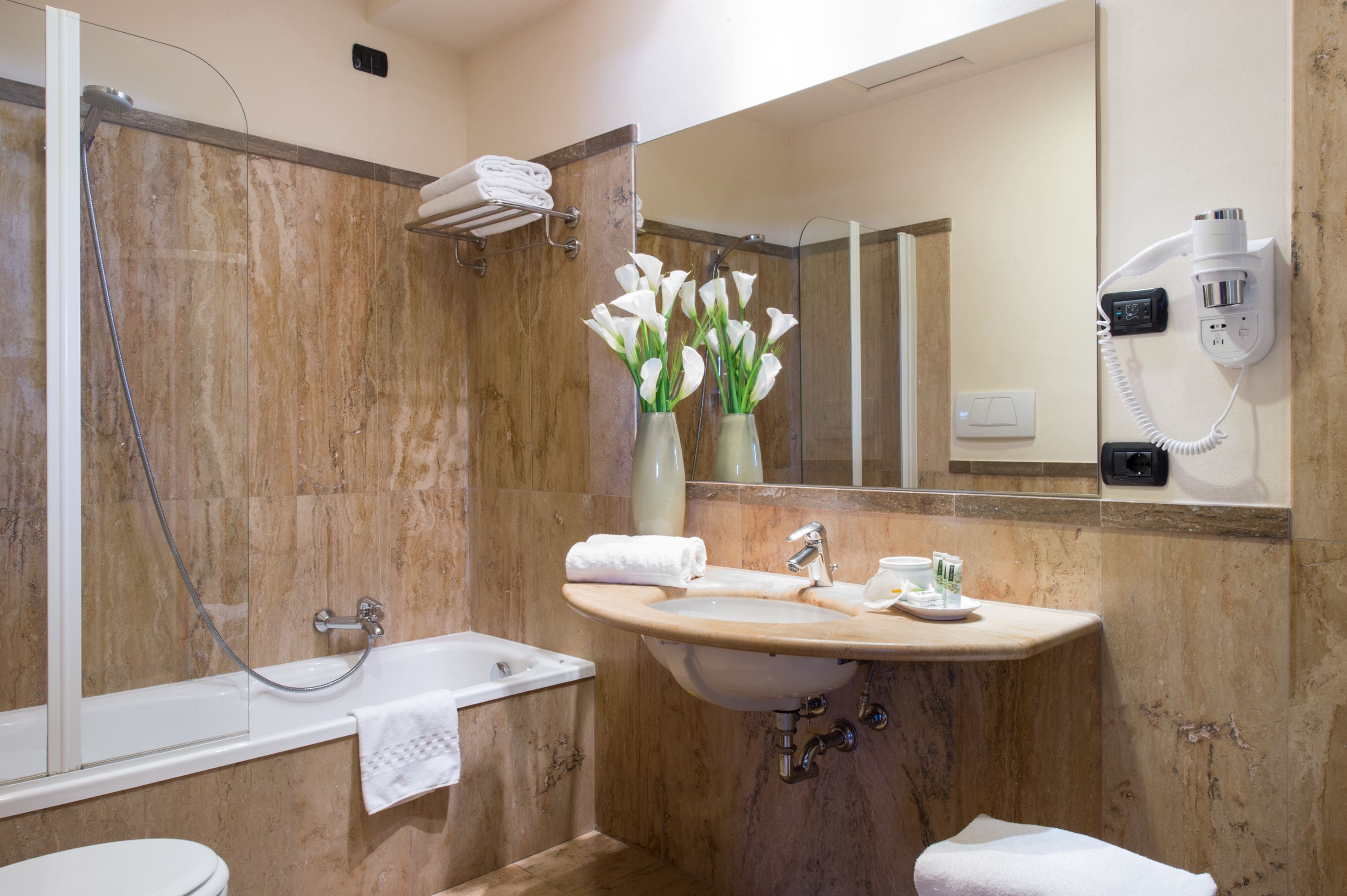 A bathroom with a bathtub, a sink, a mirror, and a hairdryer mounted on the wall.