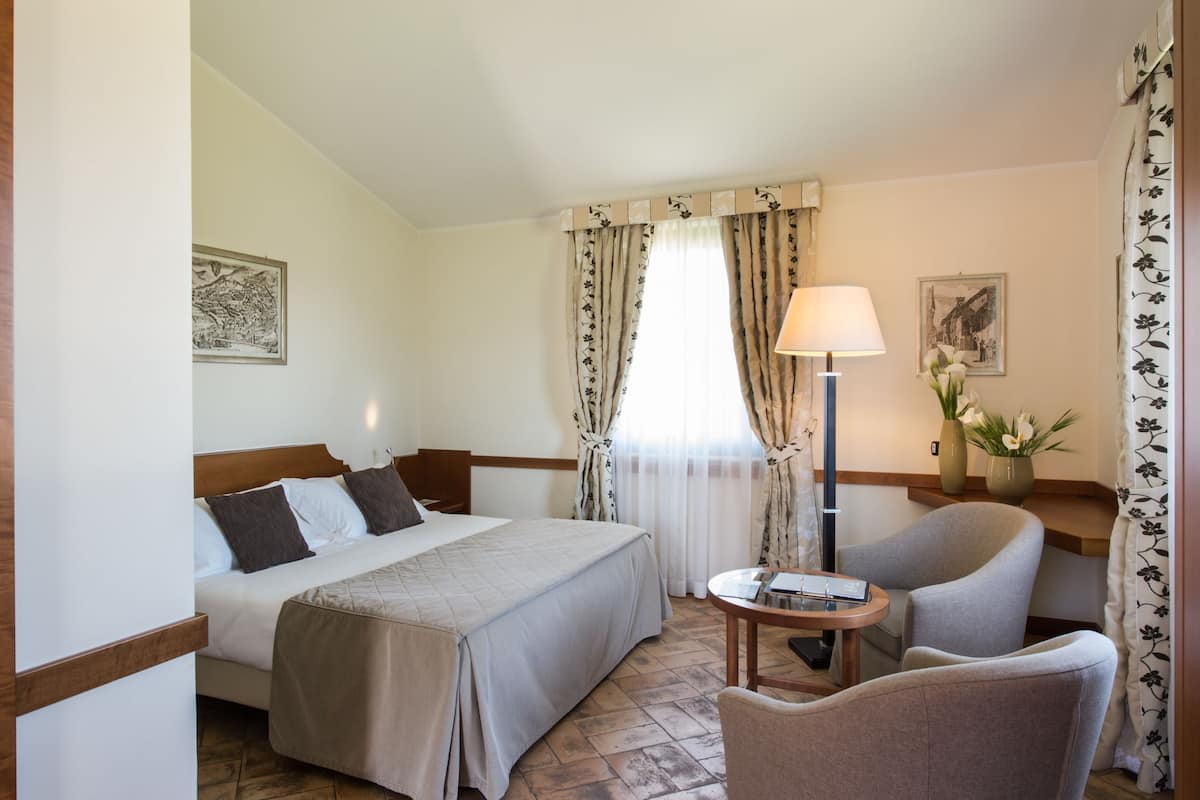 A hotel room with a bed, a chair, a lamp, and a small table.