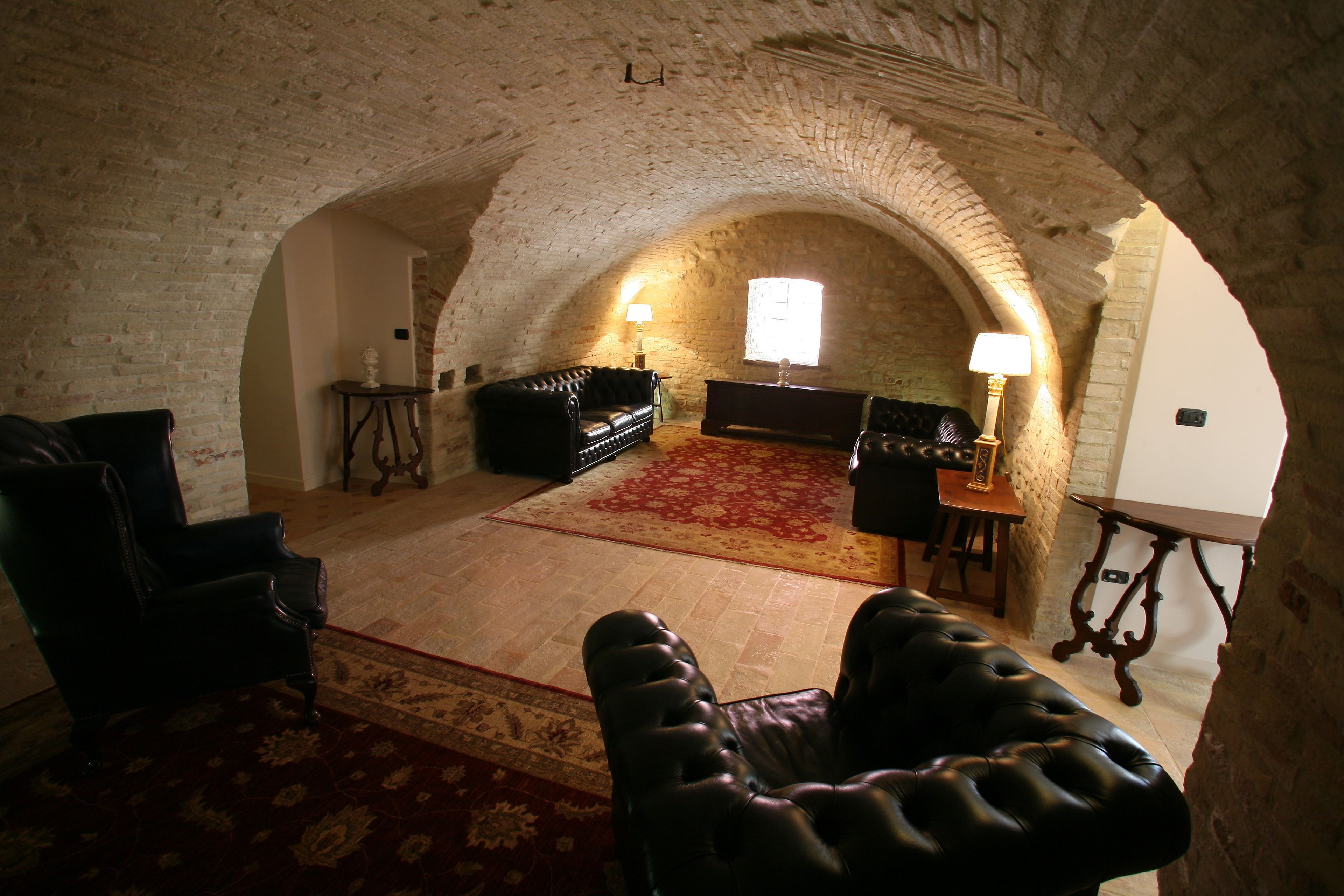 An arched room with a fireplace, leather armchairs, a red carpet, and a wooden table with a lamp.