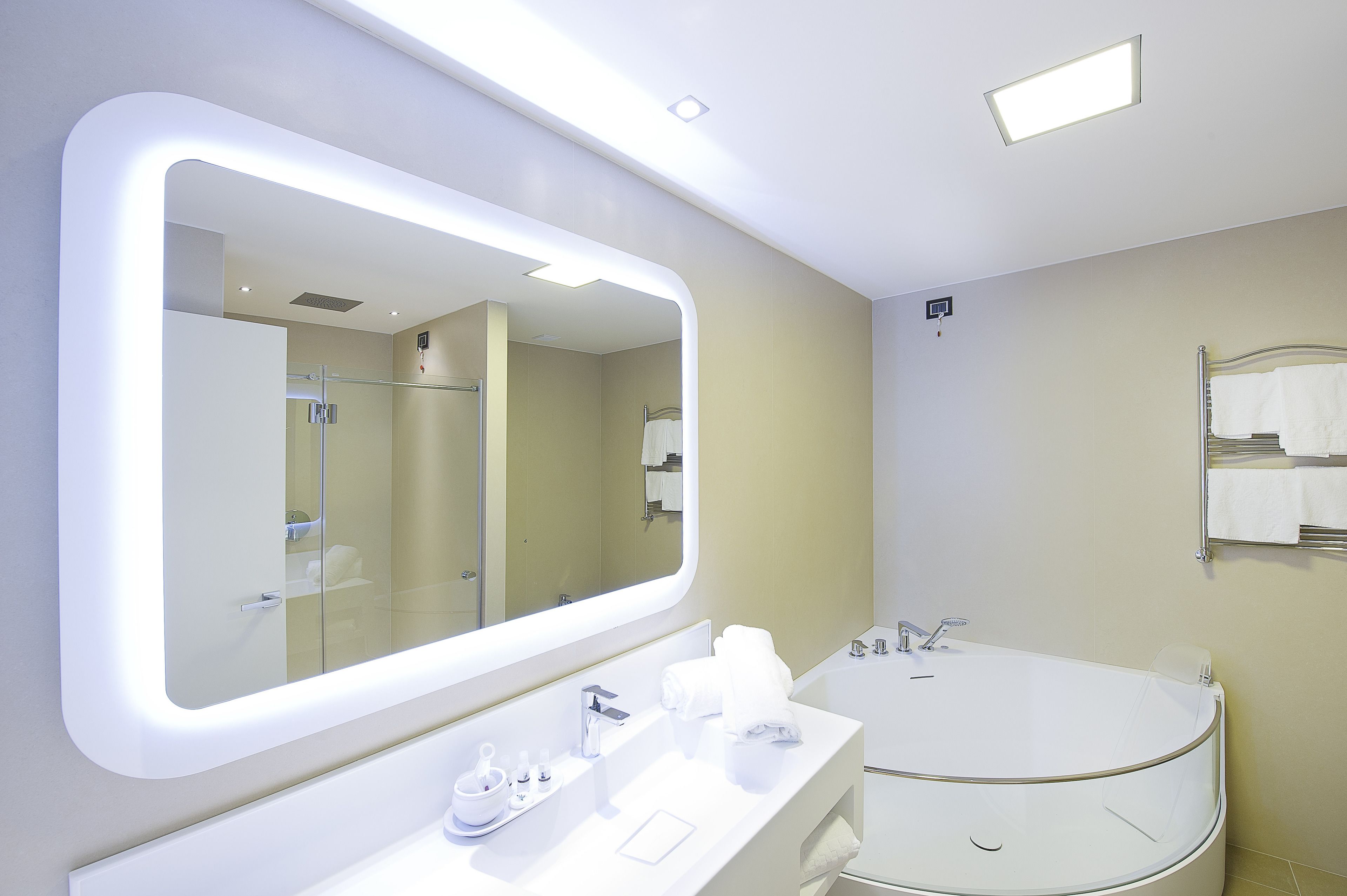 A modern bathroom with a large mirror, a round bathtub, and a vanity with toiletries.