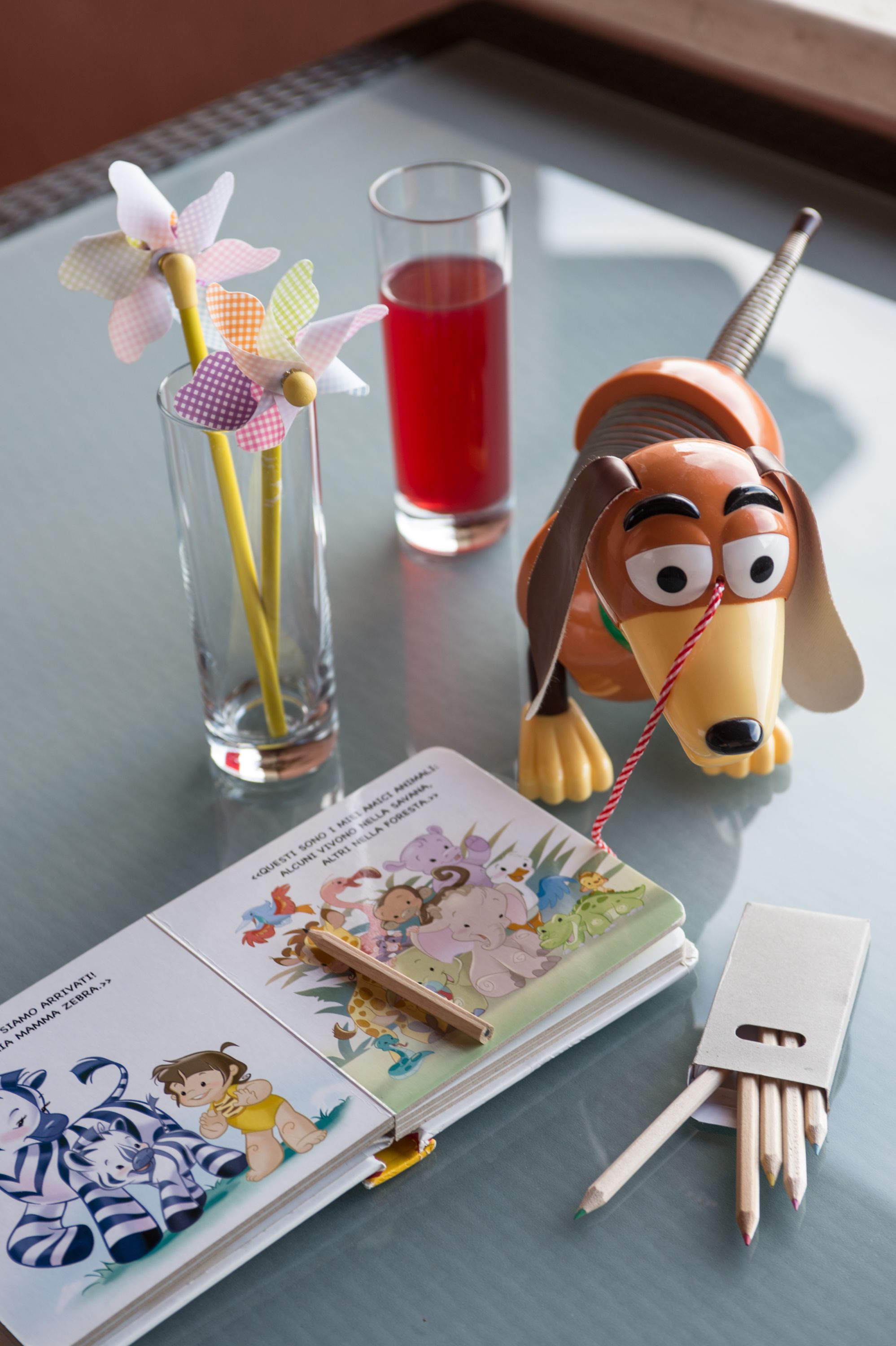Une table avec un verre contenant un liquide rouge, une figurine de chien, un livre et quelques crayons.