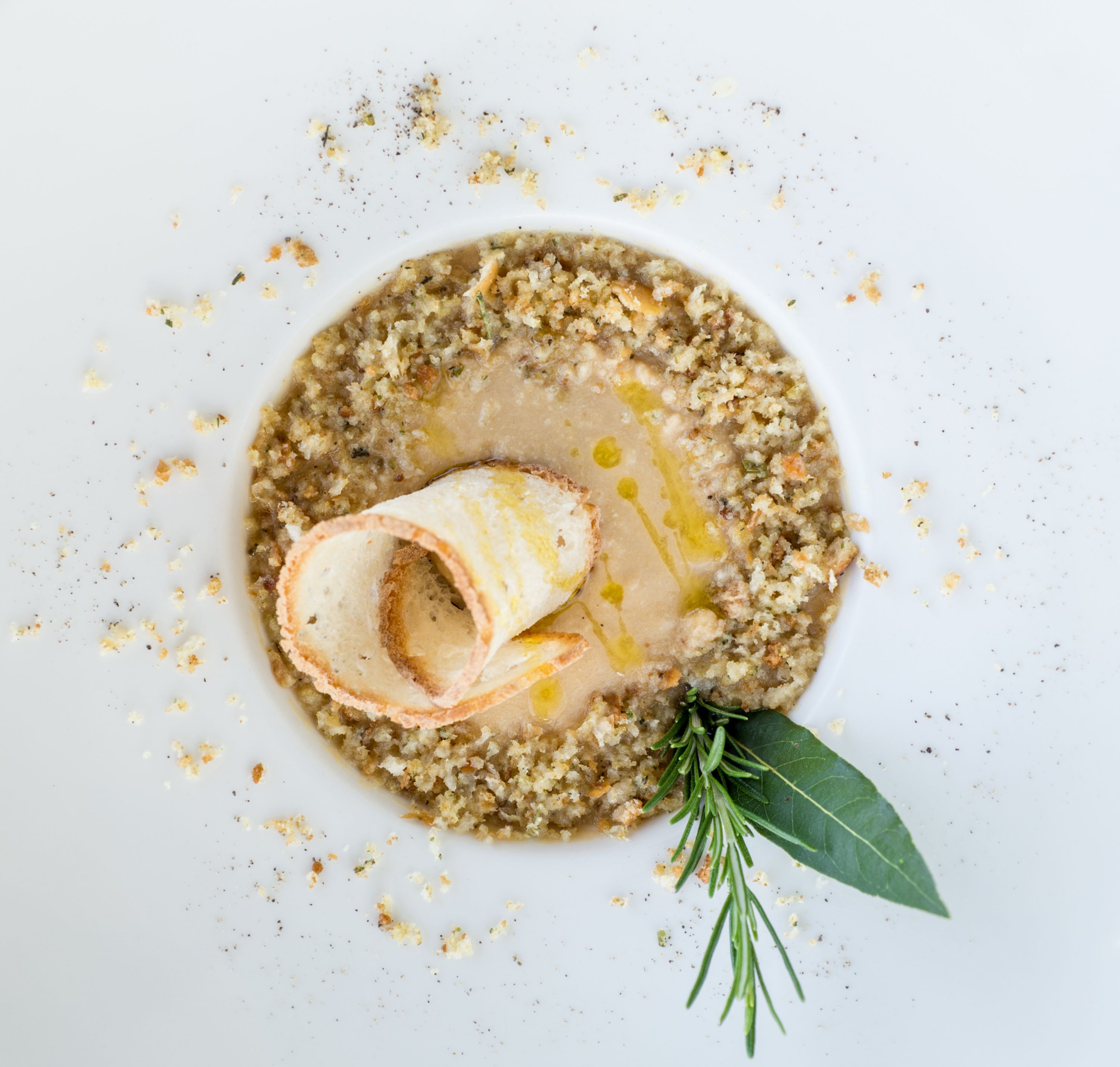 A plate with a rolled pastry, a sprig of rosemary, and scattered crumbs.