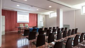 Une salle de conférence avec des rangées de chaises, un écran de présentation et une table recouverte d’une nappe bleue.