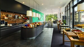 Una cafetería moderna con mostrador central, zona de estar y grandes ventanales.