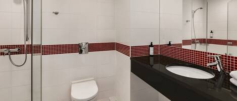 Un baño moderno con cabina de ducha de vidrio, inodoro blanco y lavabo negro con espejo superior.