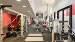 Un gimnasio con equipo de levantamiento de pesas, cintas de correr y colchonetas de ejercicio.