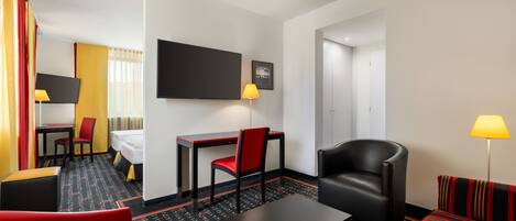 A hotel room with a bed, a desk, a chair, a sofa, and a television.