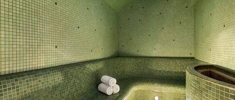 A spa room with a tiled floor and walls, a curved bench, and a small pool.
